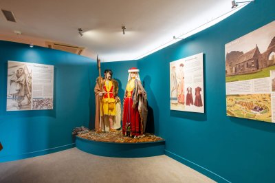 a showcase in a museum with two figures wearing ancient clothing in front of a blue wall surrounded by three different images
